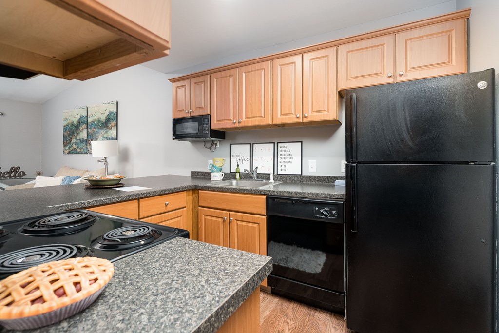 A black refrigerator sits in a kitchen with wooden cabinets.
