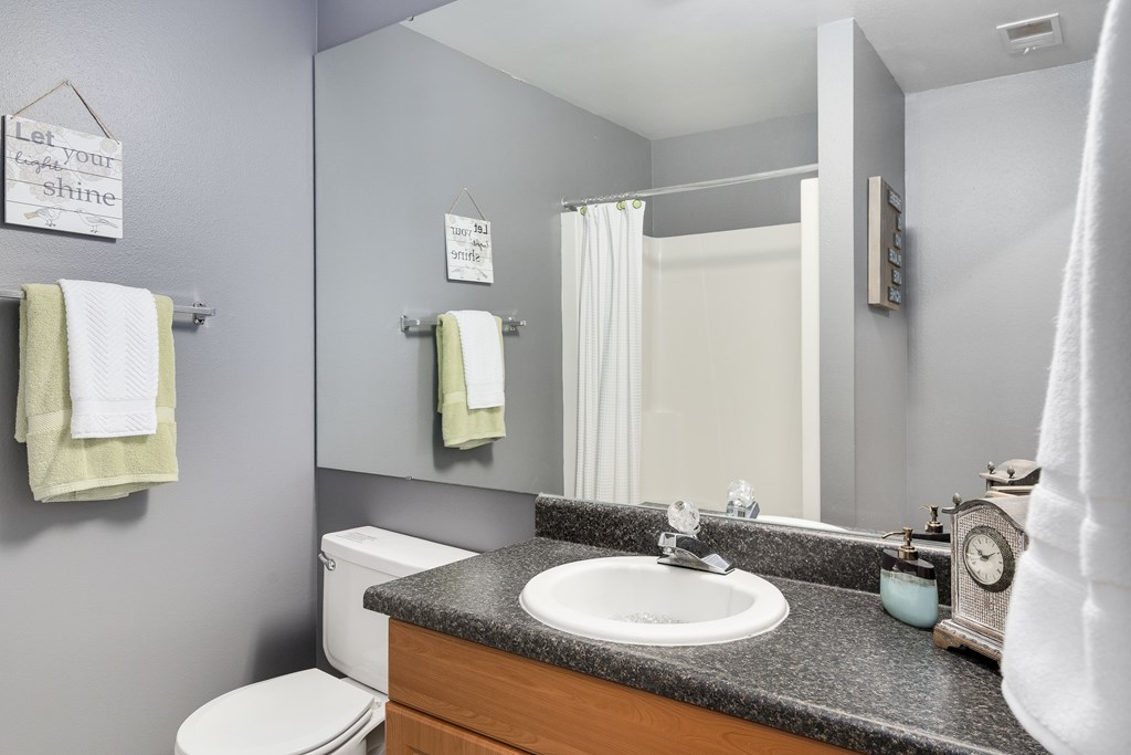 A bathroom with a toilet, sink, mirror, and towel racks.