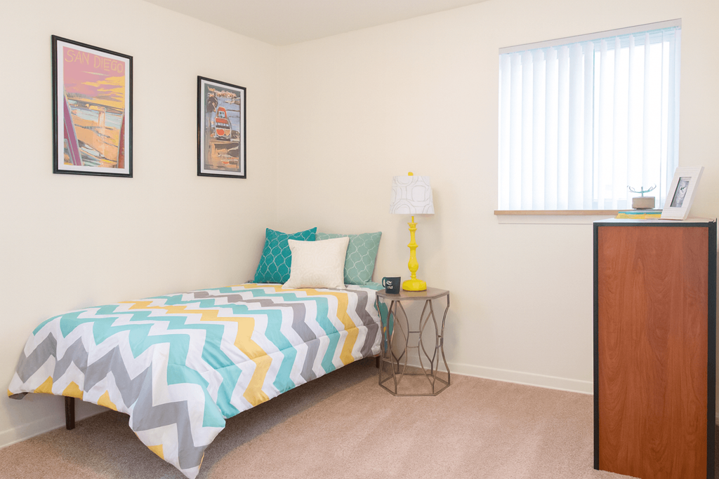 A bedroom with a bed, nightstand, and two pictures on the wall.