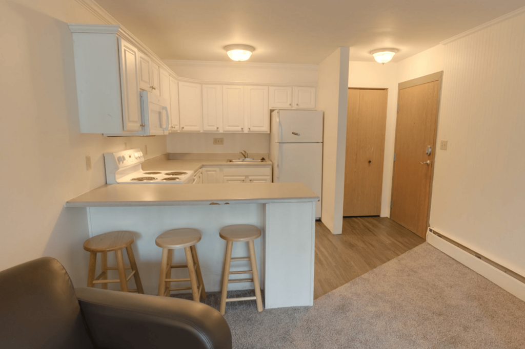 A kitchen with white appliances and wooden stools.