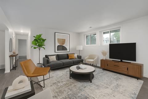 A living room with a grey couch, a brown chair, a black television and a grey rug.