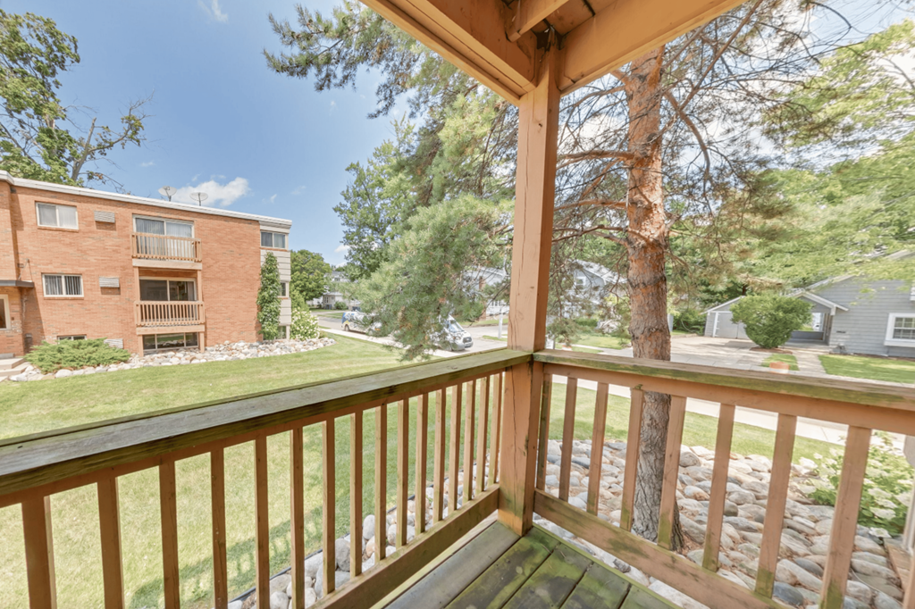 A view from a balcony looking out at a red brick building and a tree.