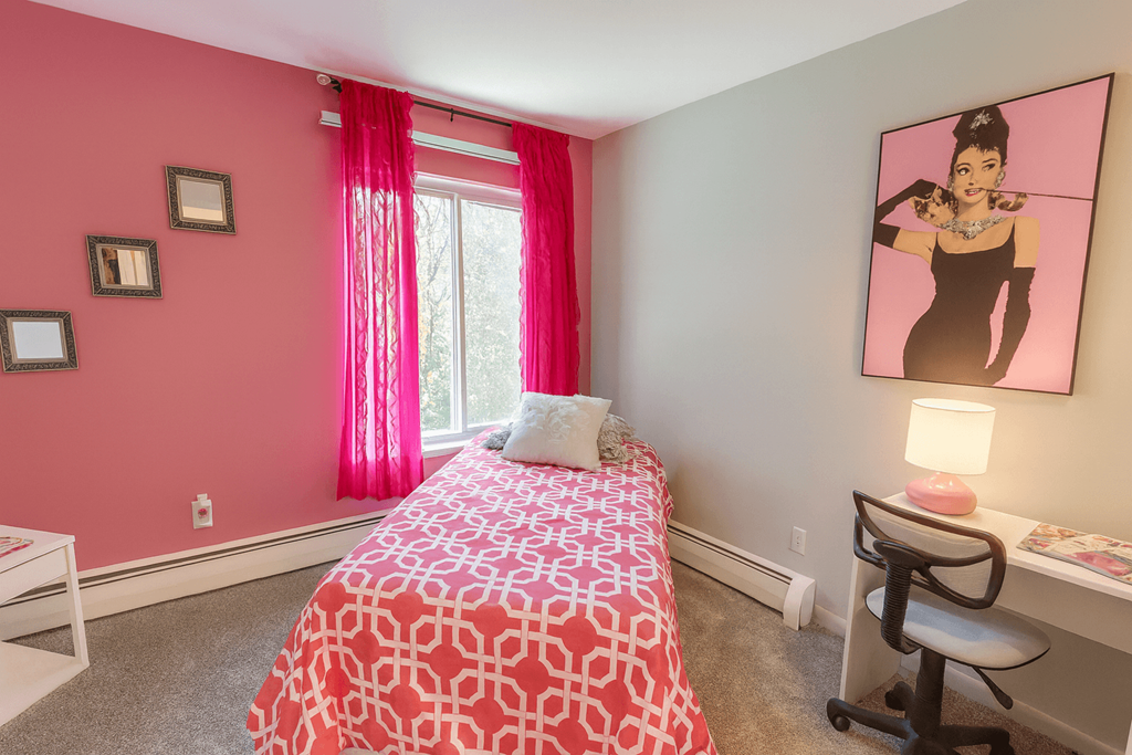 A bedroom with a pink wall and a bed with a pink and white comforter.