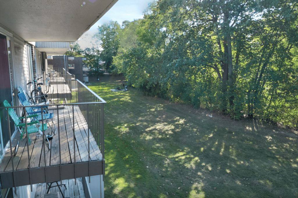 A balcony with chairs and a table overlooks a green yard.