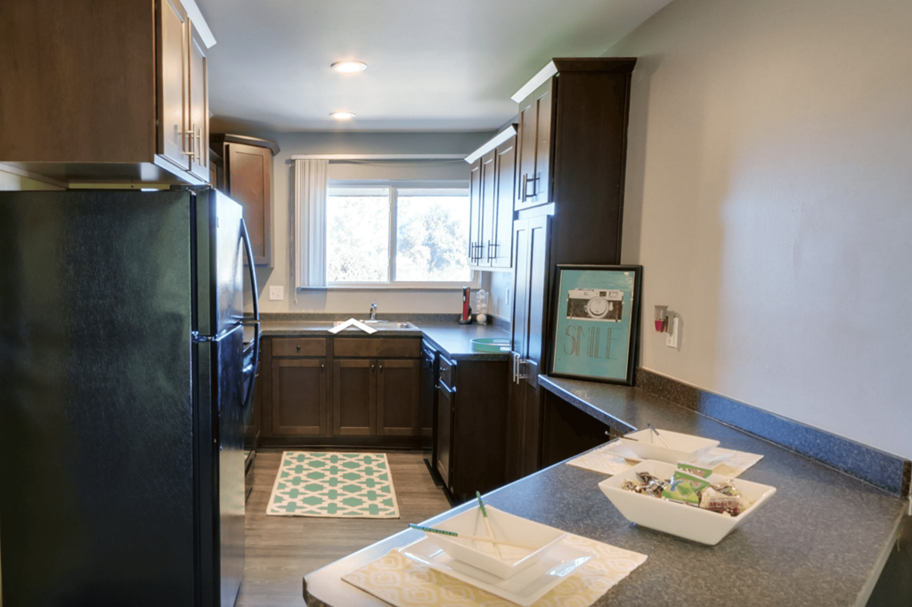 A black refrigerator is in a kitchen with brown cabinets.
