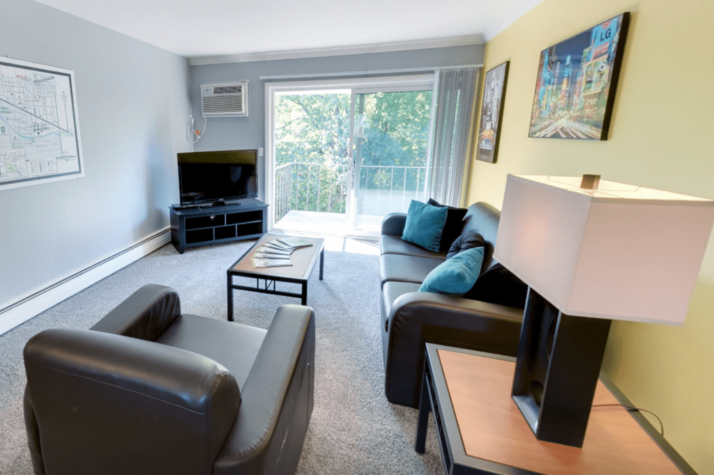 A living room with a black leather couch, a black coffee table, a black entertainment center, and a white lamp.