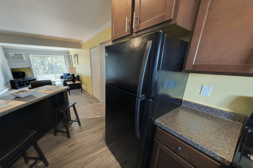 A black refrigerator is in a kitchen with wooden cabinets.