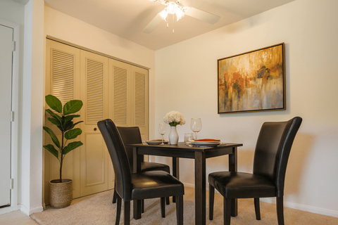 A dining room with a table set for two and a painting on the wall.