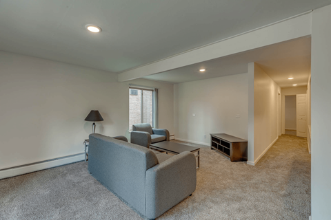 A grey couch sits in a living room with a lamp and a window.