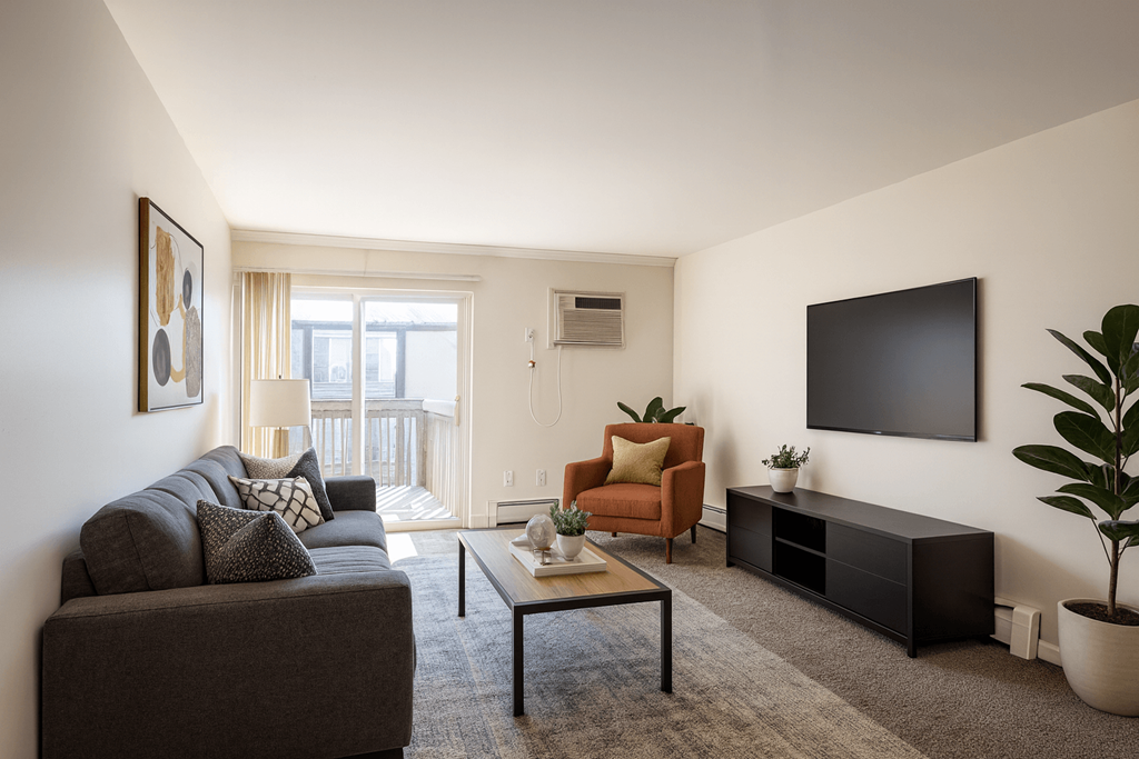 A living room with a grey couch, a brown armchair, a black coffee table, and a flat screen TV mounted on the wall.