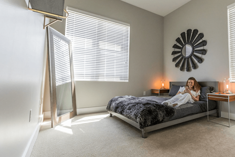 A woman is sitting on a bed in a bedroom with a large mirror on the wall.