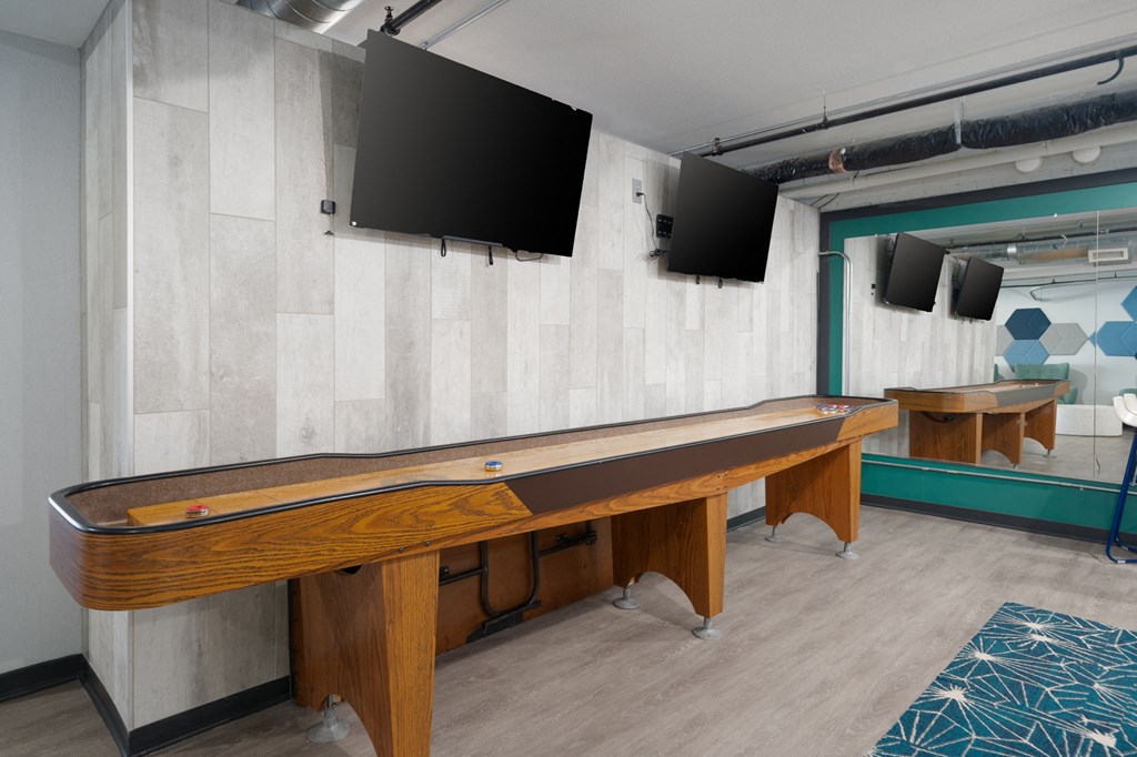 a games room with a shuffleboard table and two televisions