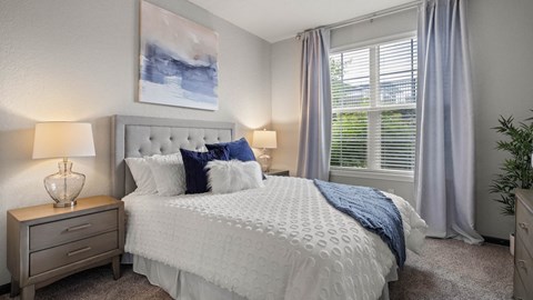 A bedroom with a large bed, a nightstand with a lamp, and a painting on the wall.