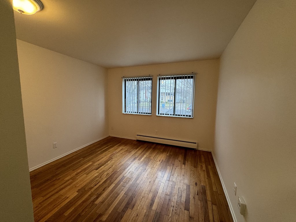 An empty living room with wooden floors and two windows
