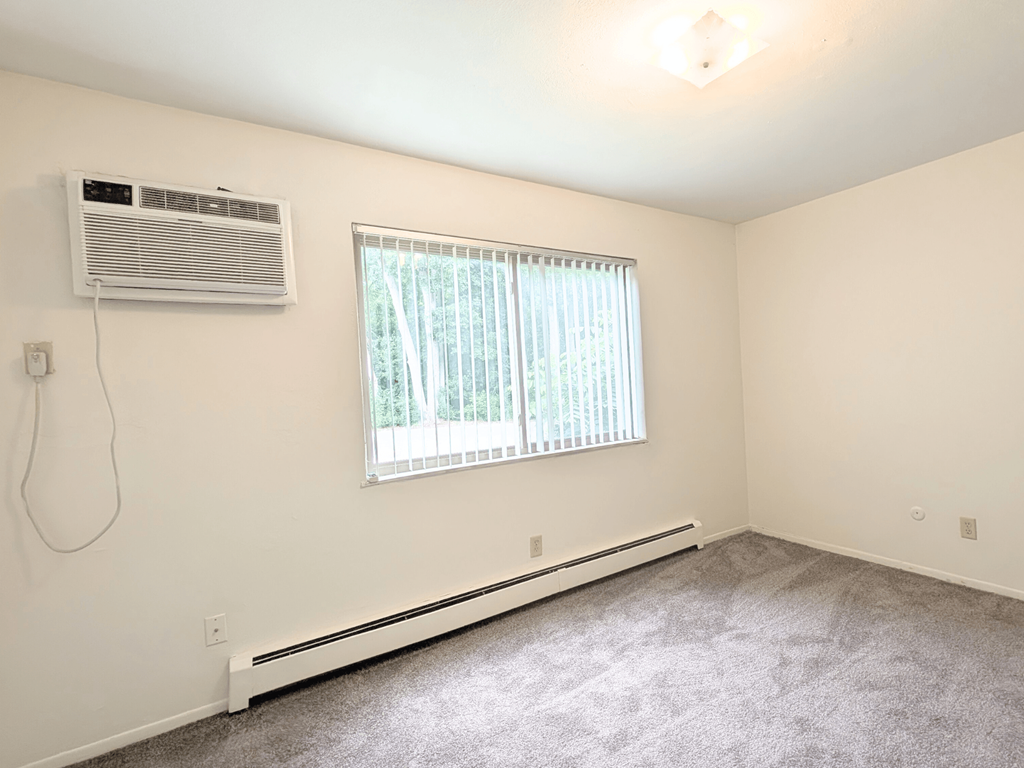 A room with a window, air conditioner, and carpeted floor.