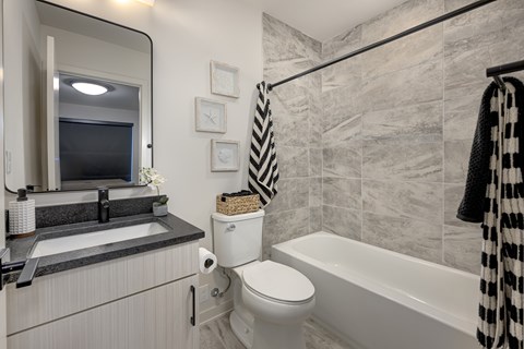 A bathroom with a white toilet, a white bathtub, and a black and white striped towel.