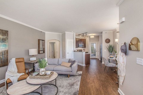 a living room with a couch table and chairs and a kitchen in the background