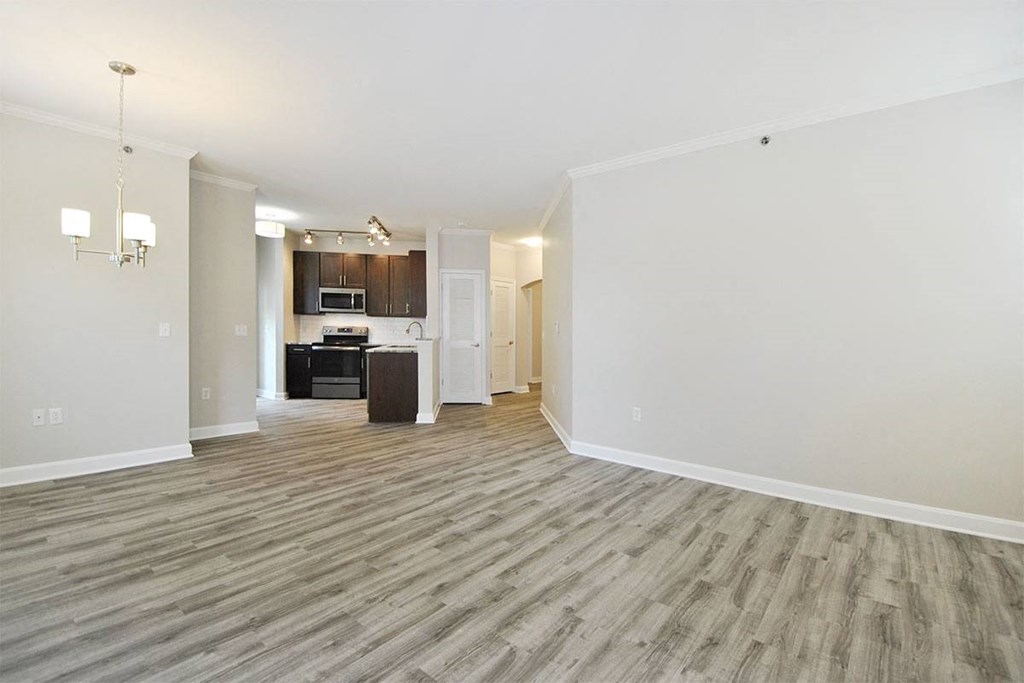 an empty living room with a kitchen in the background