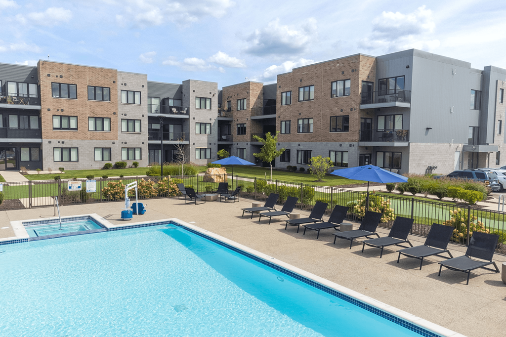 A swimming pool surrounded by lounge chairs and umbrellas in front of apartment buildings.