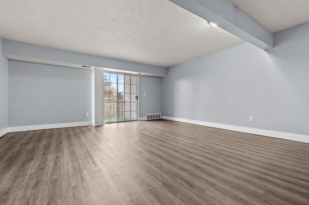 an empty living room with wood flooring and a door to a balcony