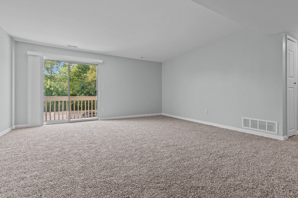 an empty living room with carpet and a door to a balcony