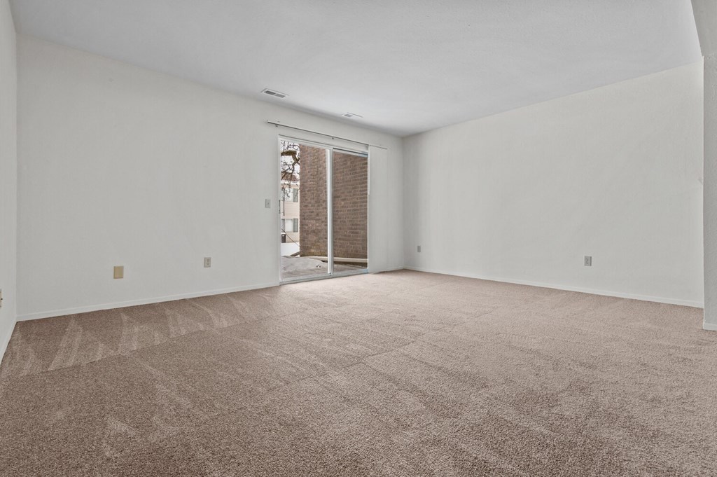 a living room with white walls and carpet and a sliding glass door