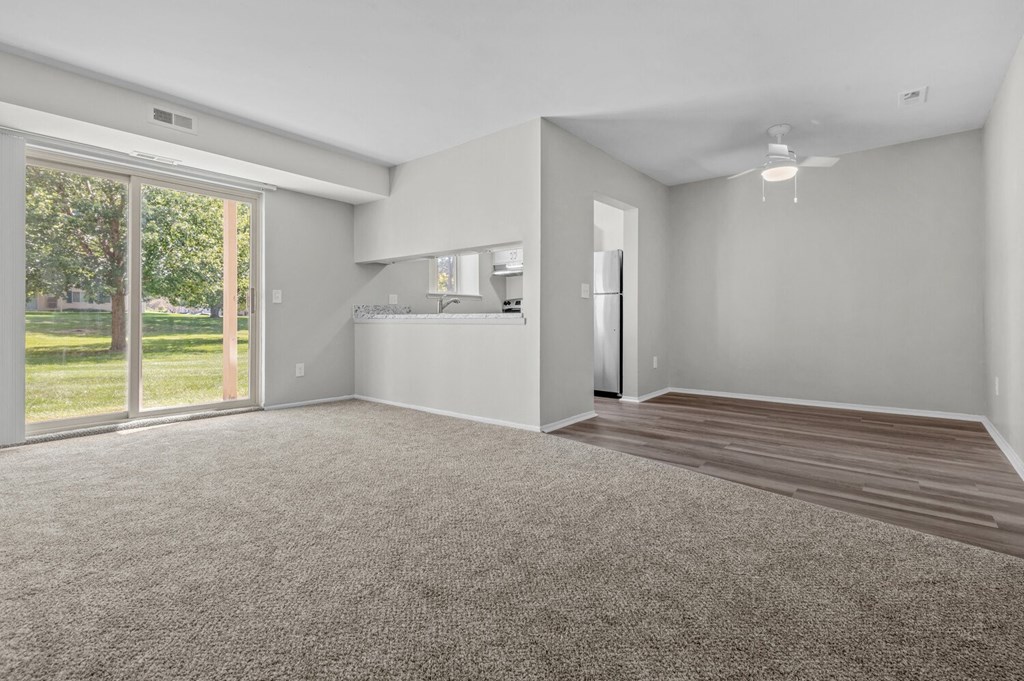an empty living room with a large window and a kitchen