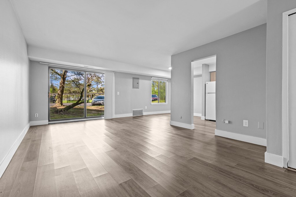 A spacious room with wooden flooring and a view of the outdoors through a sliding glass door.