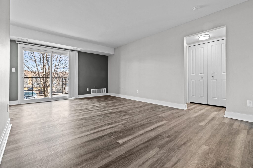 an empty living room with a large window and a door to a balcony at Sunnymede Apartments - Troy, MI, Troy, 48084