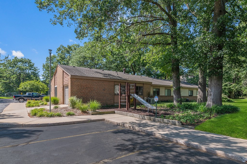 a small brick house with trees and a driveway