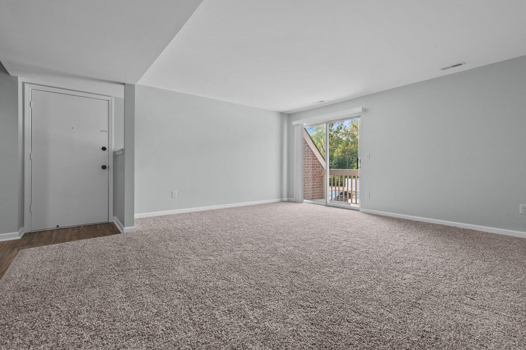 an empty living room with carpet and a door to a balcony