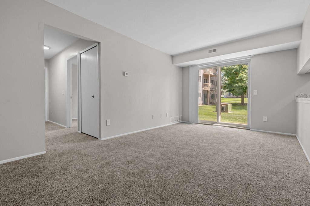 the living room of an apartment with carpet and a door to the yard