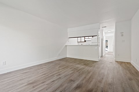an empty living room and kitchen with white walls and wood flooring