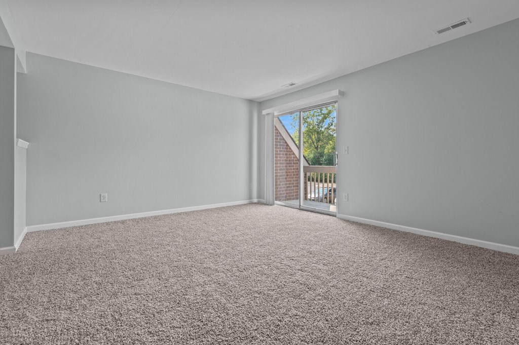 an empty living room with a sliding glass door to a balcony