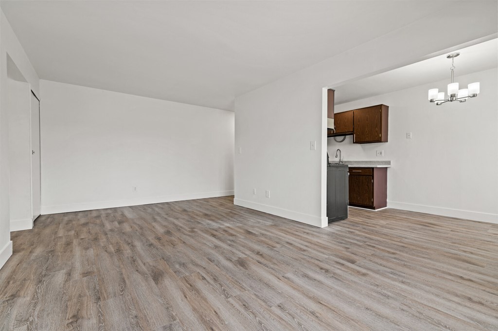 an empty living room with wood flooring and a kitchen