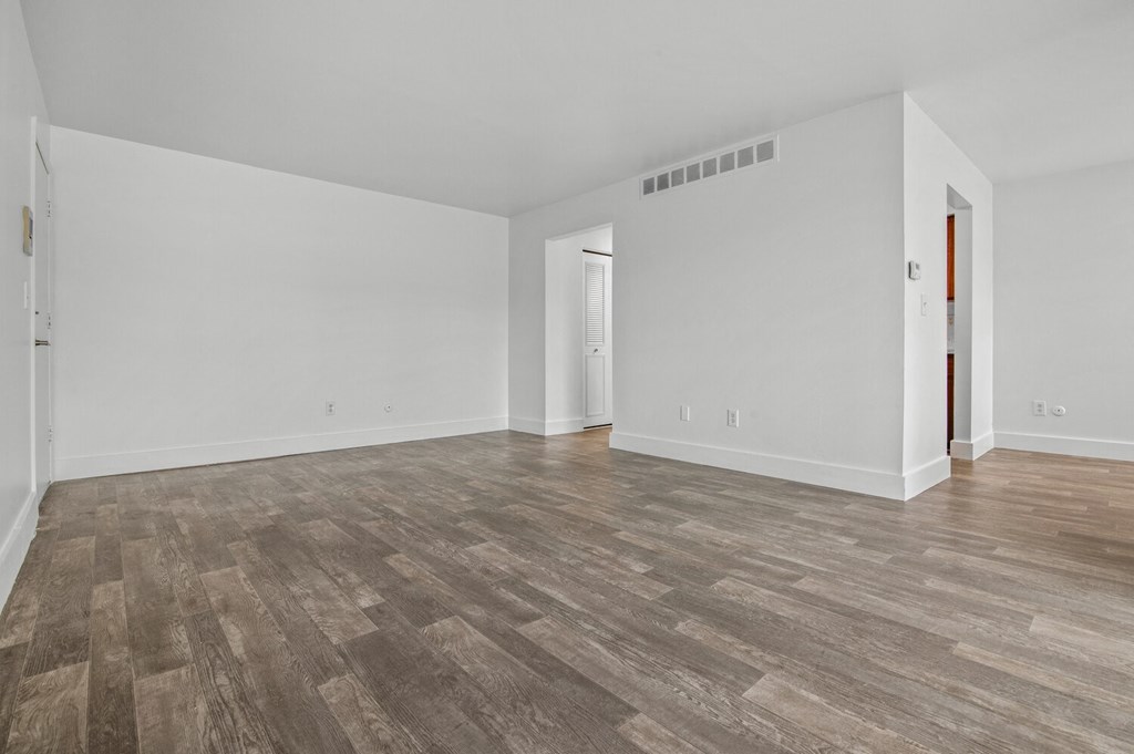 the living room of an apartment with white walls and wood floors