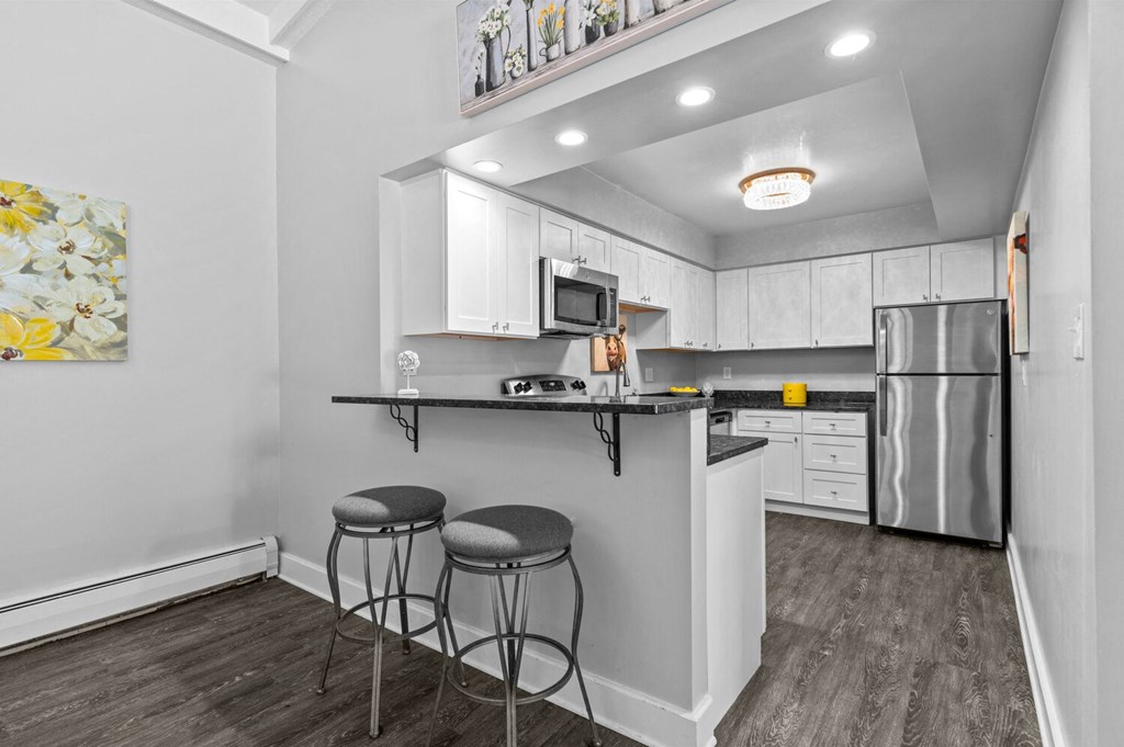 a kitchen with white cabinets and a black counter top with two stools at Apple Ridge Apartments - Livonia, MI, Livonia, 48152