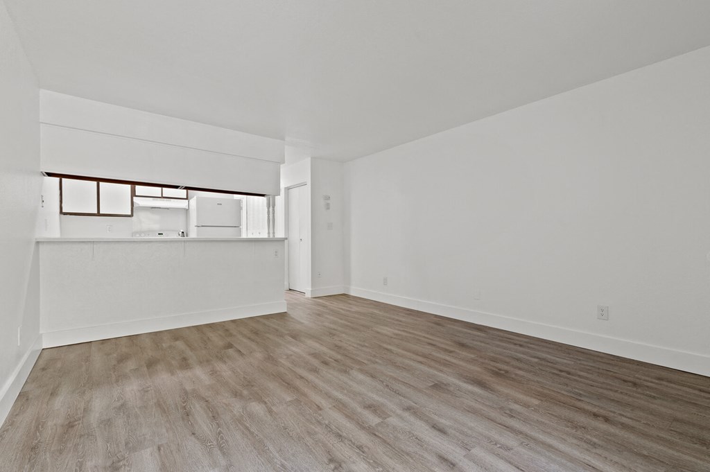 an empty living room and kitchen with white walls and wood flooring