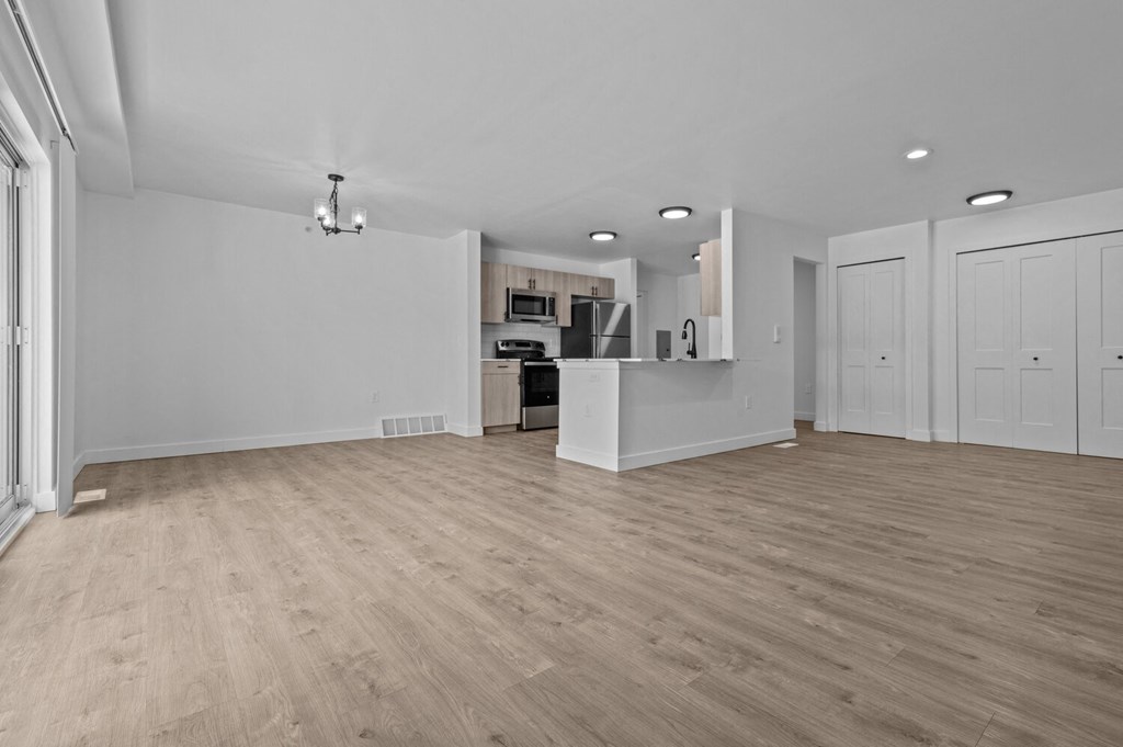 an empty living room and kitchen with white walls and wood flooring