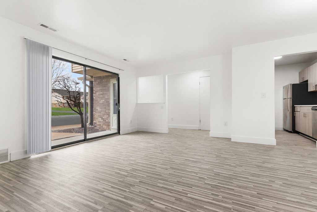 an empty living room with a sliding glass door to a kitchen