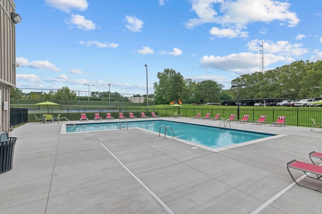 a swimming pool with chairs around it and a grassy field in the background