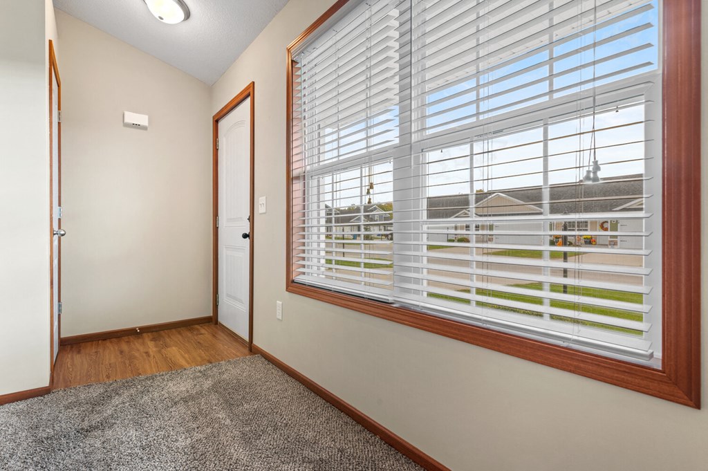a bedroom with a large window with white blinds and a door to a hallway