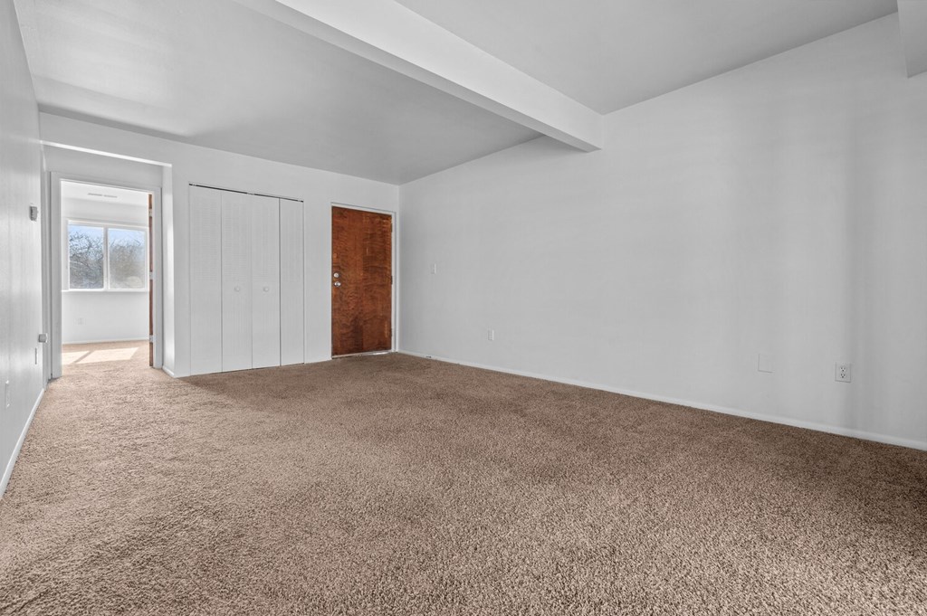 an empty living room with carpet and a door to a bedroom