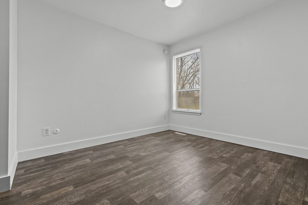 a bedroom with white walls and wood flooring and a window
