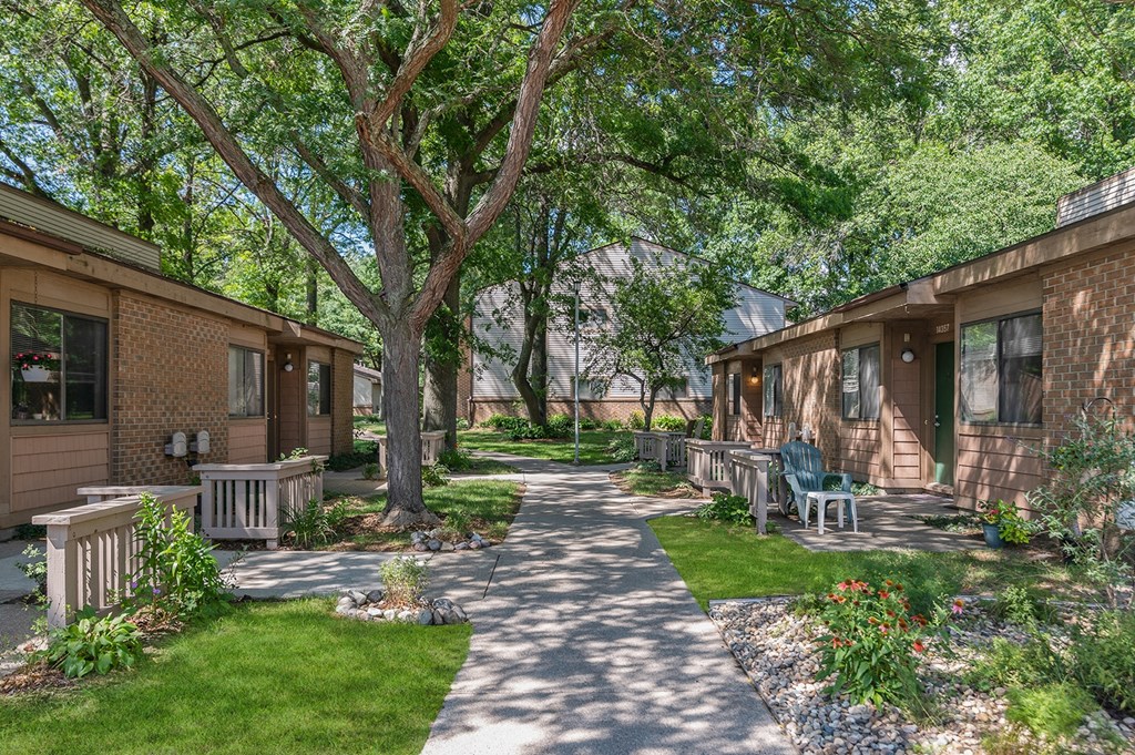 a walkway between two houses with trees and benches