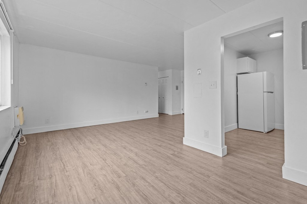 the living room and kitchen of an apartment with white walls and wood flooring