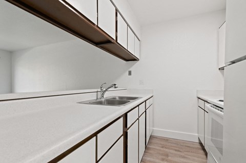 an empty kitchen with white counter tops and a sink