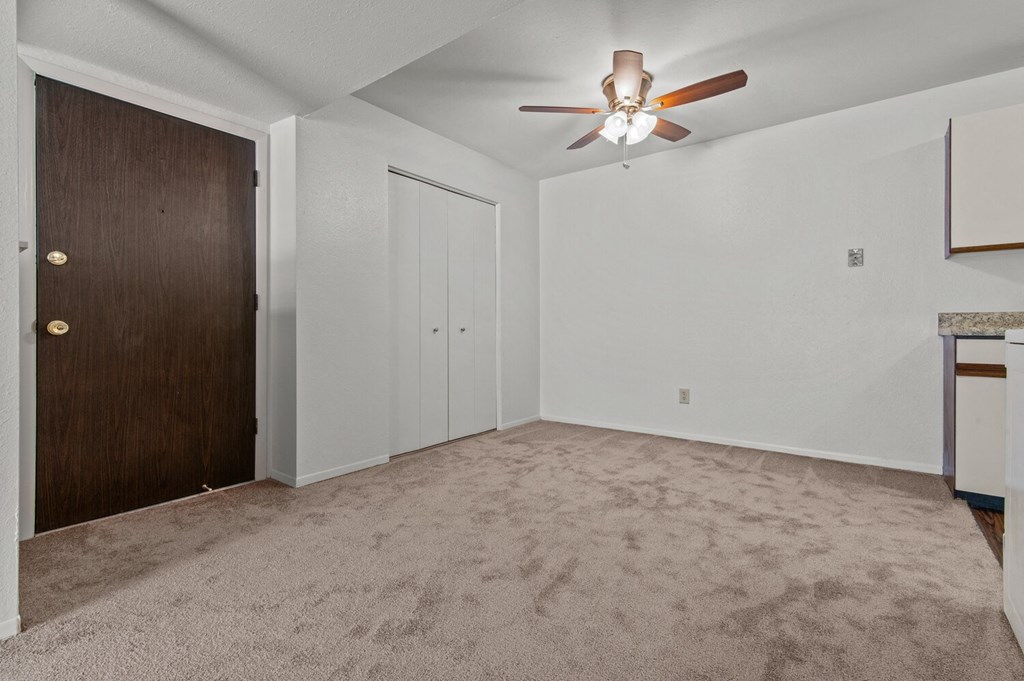 an empty living room with a ceiling fan and a door to a closet