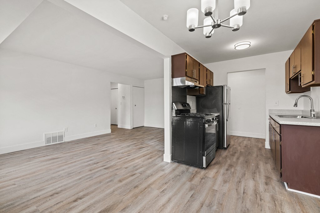 an empty living room with a kitchen with a stove and refrigerator