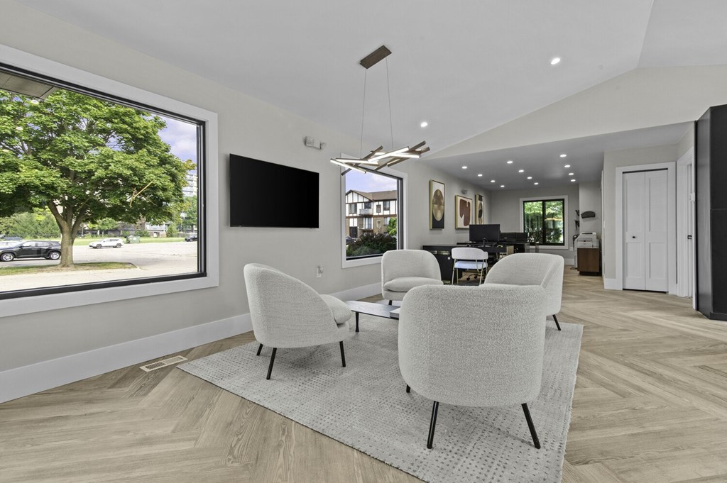 A modern living room with a large window, a flat screen TV, and a set of white chairs.